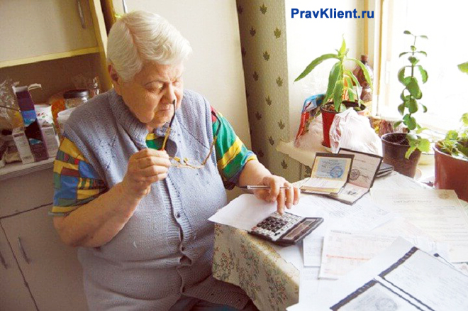 Пенсионерка за кухонным столом разбирается в платежных документах