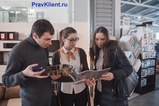 Продавец показывает покупателям каталог мебели