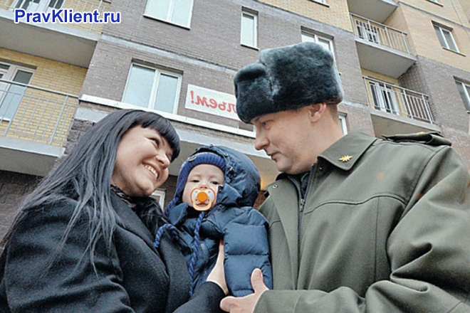 Военнослужащий стоит с семьей на фоне дома