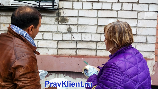 Женщина и мужчина фиксируют трещину на фасаде дома