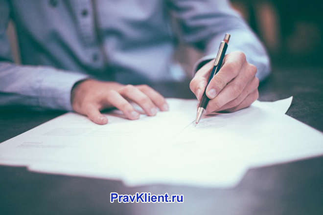 Мужчина в синей рубашке пишет на листке бумаги